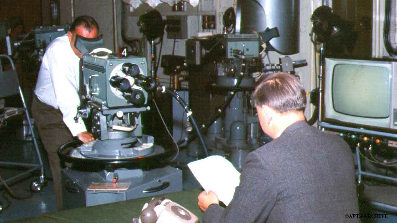 News reader at his desk in preparation for the news program. In the background can be seen a variety of cameras and studio equipment. Studio B, Alexandra Palace.