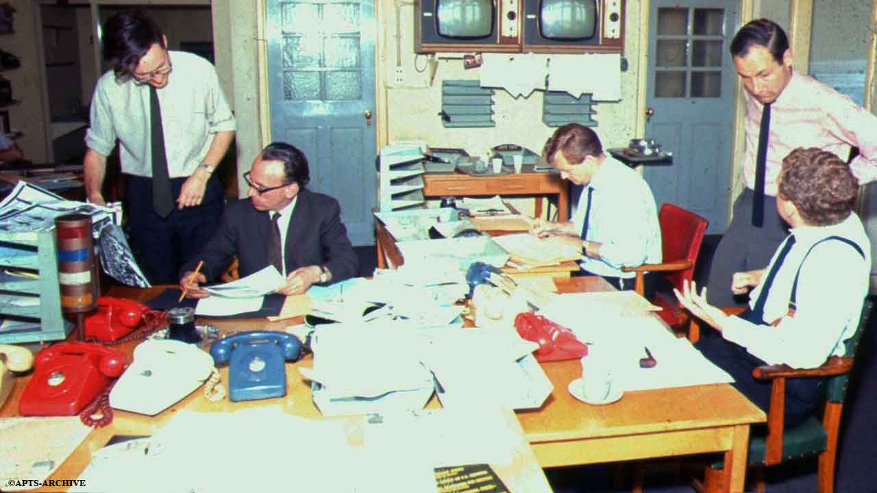 Photograph circa 1964/5. Roger Wilson, from the Photograph Library (far left) can be seen discussing a photograph for a news story, with the Duty Editor. This is the opposite view of above photograph, showing two televisions for viewing the various news bulletins transmitted on BBC1 and on BBC2.