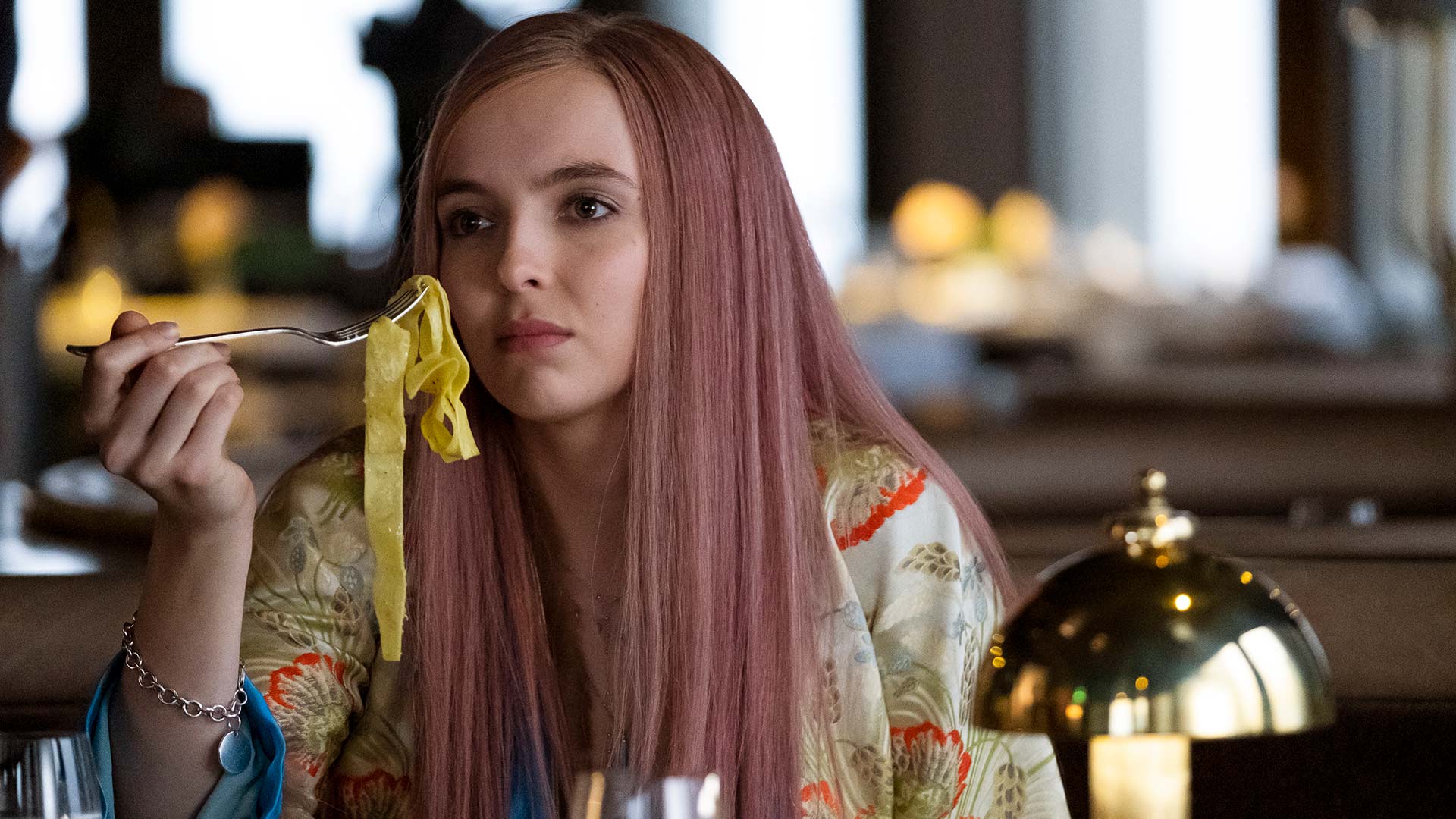 Killing Eve Season 2 (2019). Villanelle, who is wearing a pink wig and a silk jacket, holds a forkful of creamy tagliatele up to her mouth.