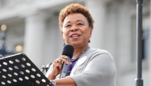 Barbara Lee, an African American woman, speaking at a podium with a microphone.