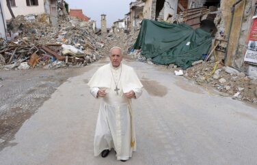 Man (Pope Francis) stands on a street with a lot of rubble in the background.