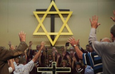 Congregation in a Jewish temple with arms held up.